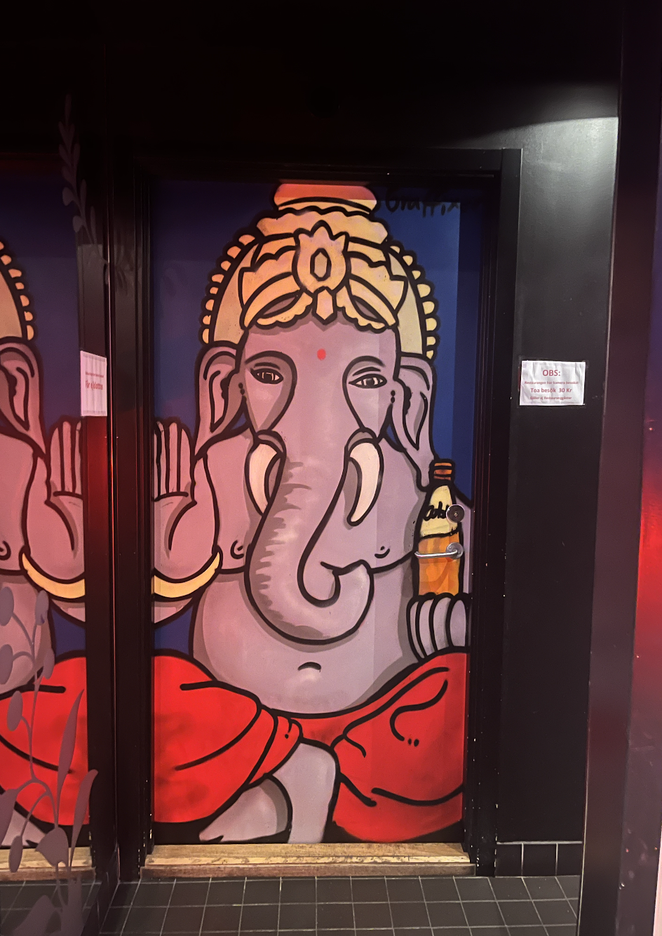 A graffiti painted door by Graffiter to Spice graden in Stockholm. Colorful mural of Lord Ganesha painted on a door, featuring large ears, trunk, and red clothing, with a small bottle drawn on the right side.