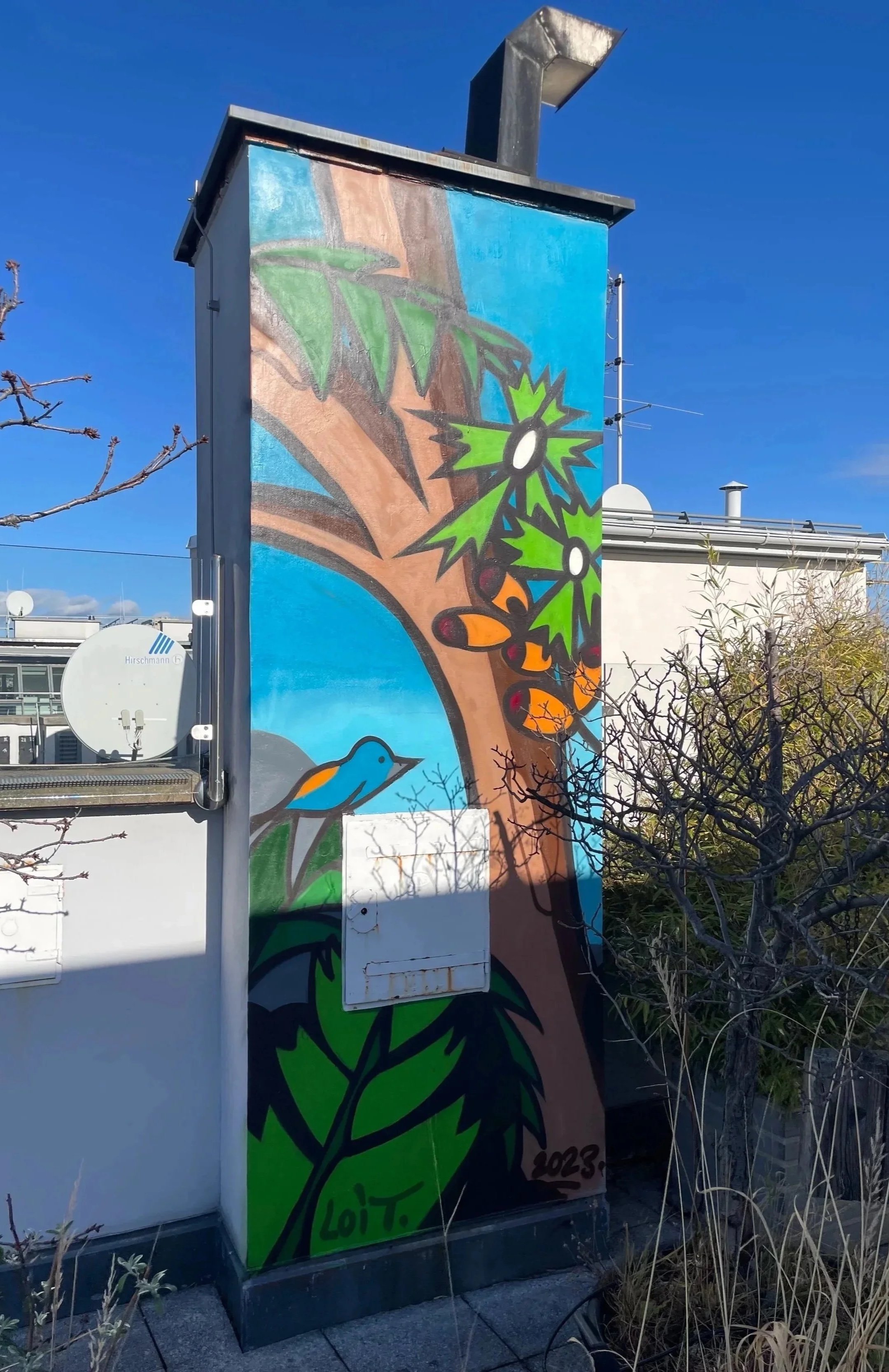 Colorful mural painting of a tree with green leaves on an electrical box, featuring a bluebird perched at the bottom, with a background of blue sky and house rooftops.
