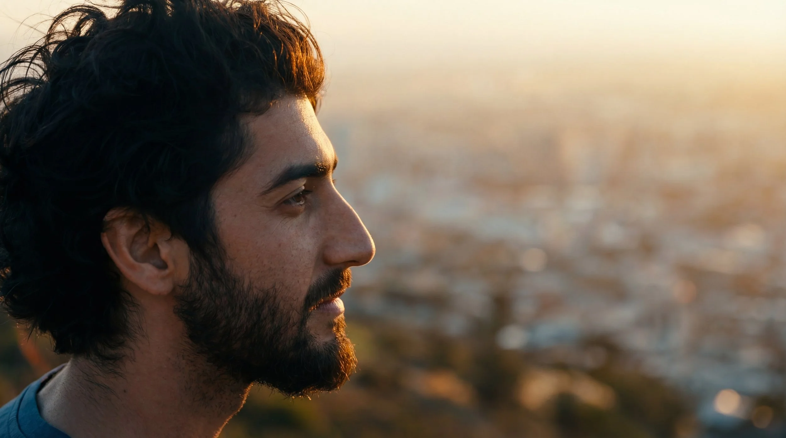 Side profile of a man with dark curly hair and a beard, looking towards the horizon during sunset. Julien Maalouf