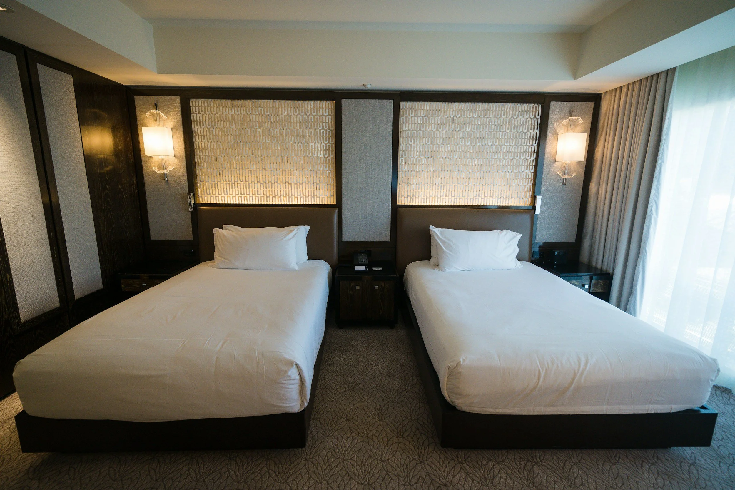 Hotel room with two twin beds, nightstands, wall-mounted lamps, and curtains.