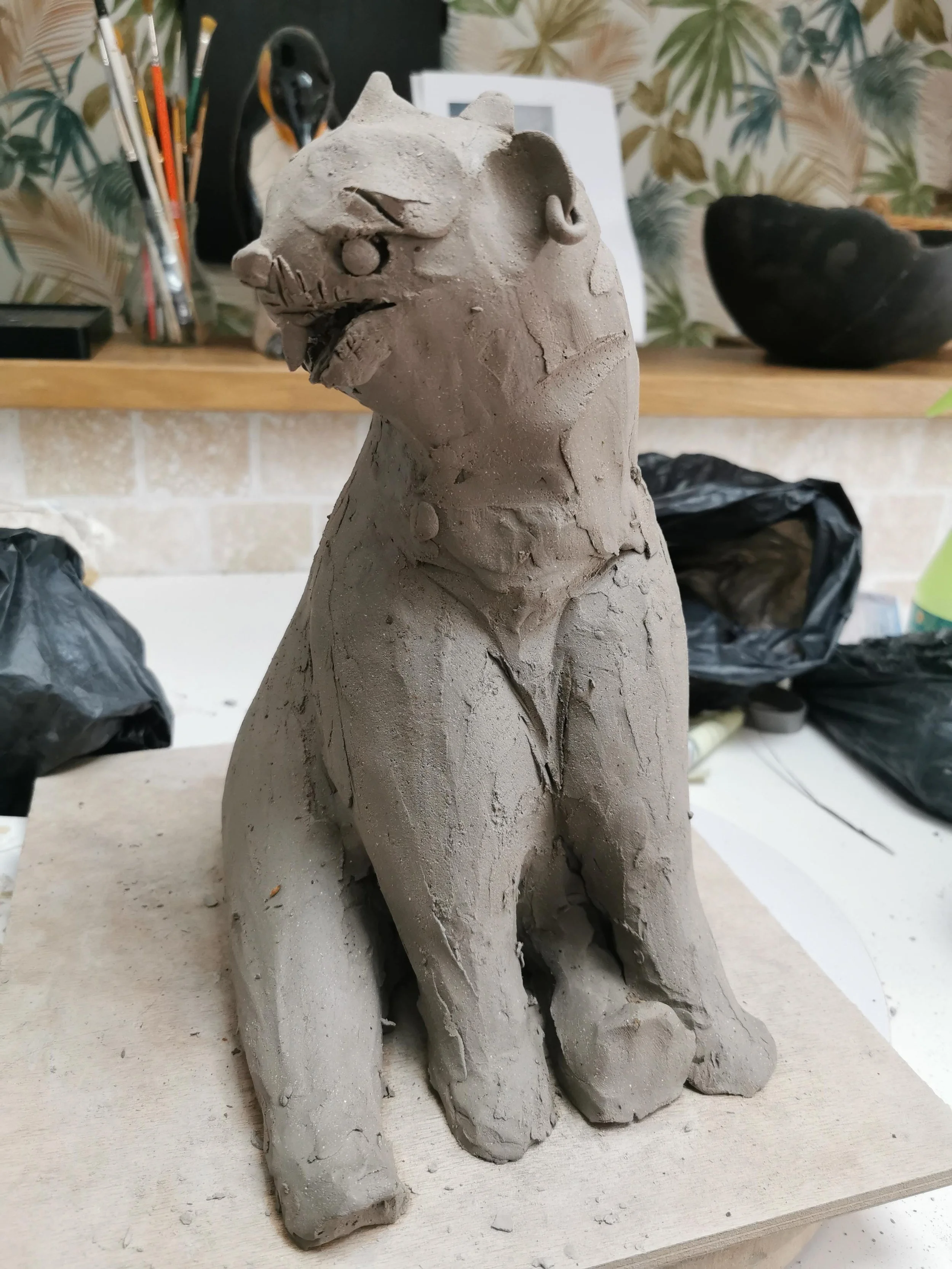 Sculpture en argile d'un ours assis, avec des détails sculptés pour représenter les traits du visage et la posture.