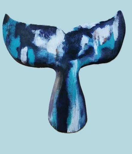 Une sculpture abstraite en métal représentant une queue de cachalot stylisée, peinte en nuances de bleu, gris et blanc, sur un fond bleu clair.