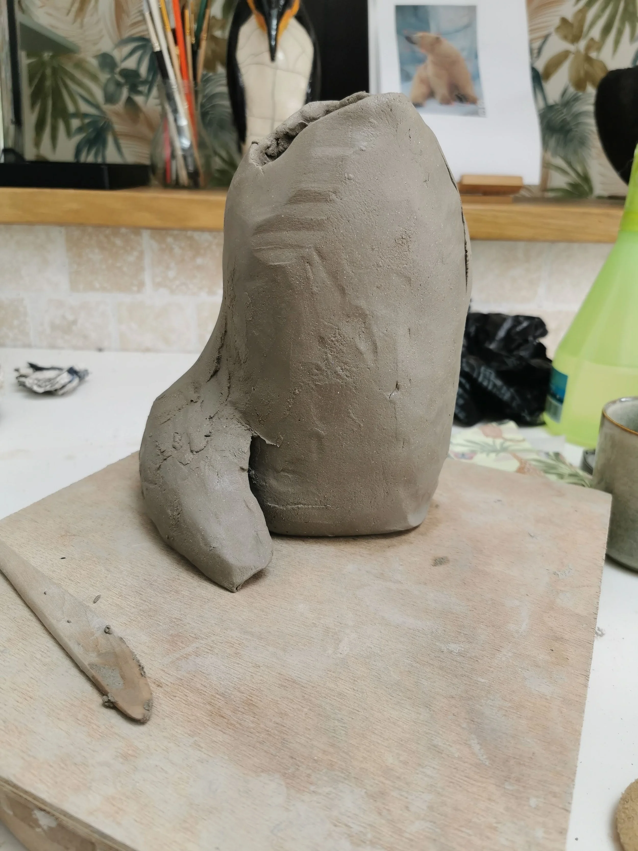 Une sculpture en argile en cours de création, placée sur une planche en bois.