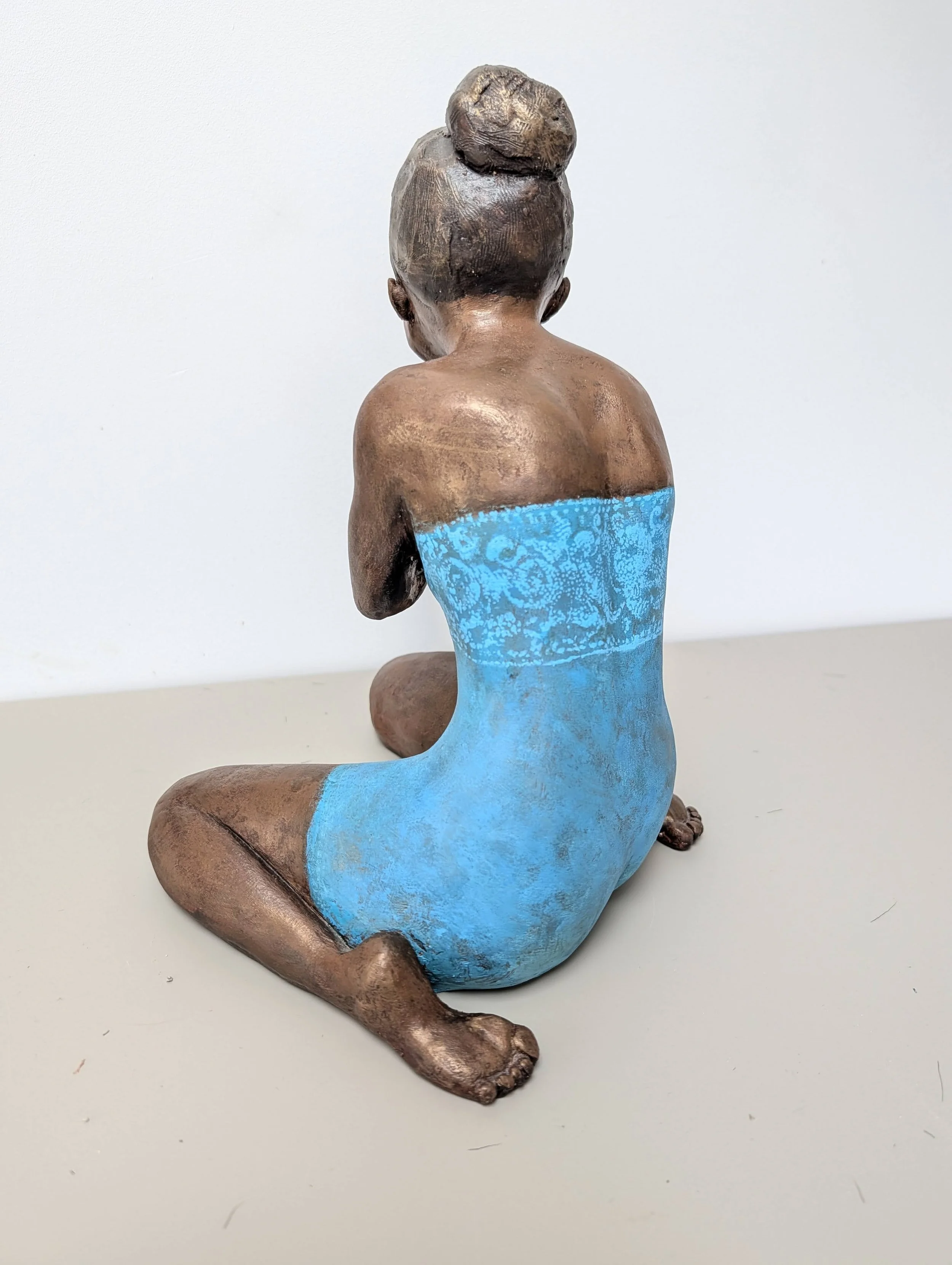 Statue en céramique d'une femme assise à genoux portant un vêtement bleu clair, vue de dos.