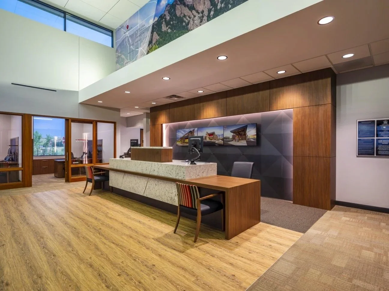 Modern lobby with a reception desk, wooden accents, and multiple monitors on the wall.