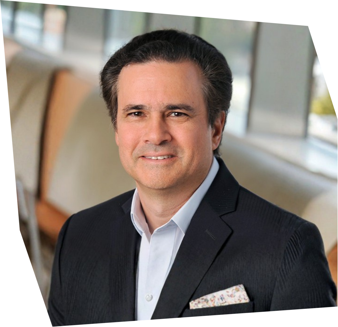 Close-up photo of a white man with short hair, wearing a black suit, looking directly at the camera.