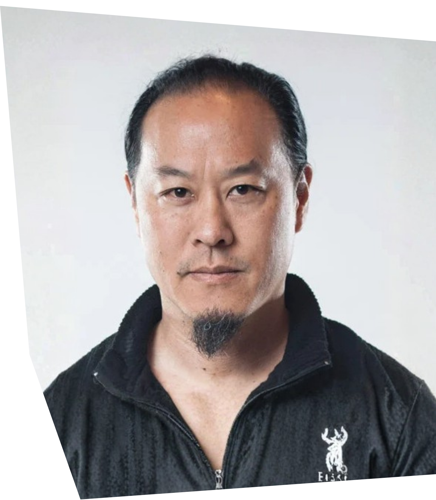 Close-up of a young man with dark hair in a black turtleneck, looking off to the side against a cloudy sky, outdoor setting.