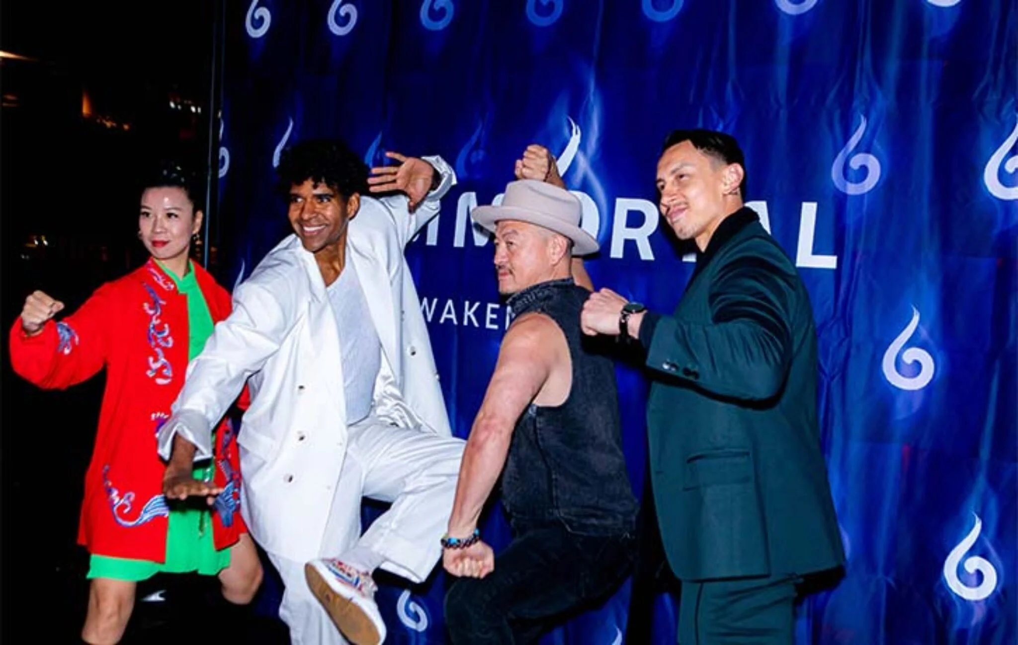 Five diverse individuals posing and interacting in a lively scene against a blue backdrop with the word 'Awakening' visible. The group displays energetic and friendly gestures, expressing excitement and camaraderie.