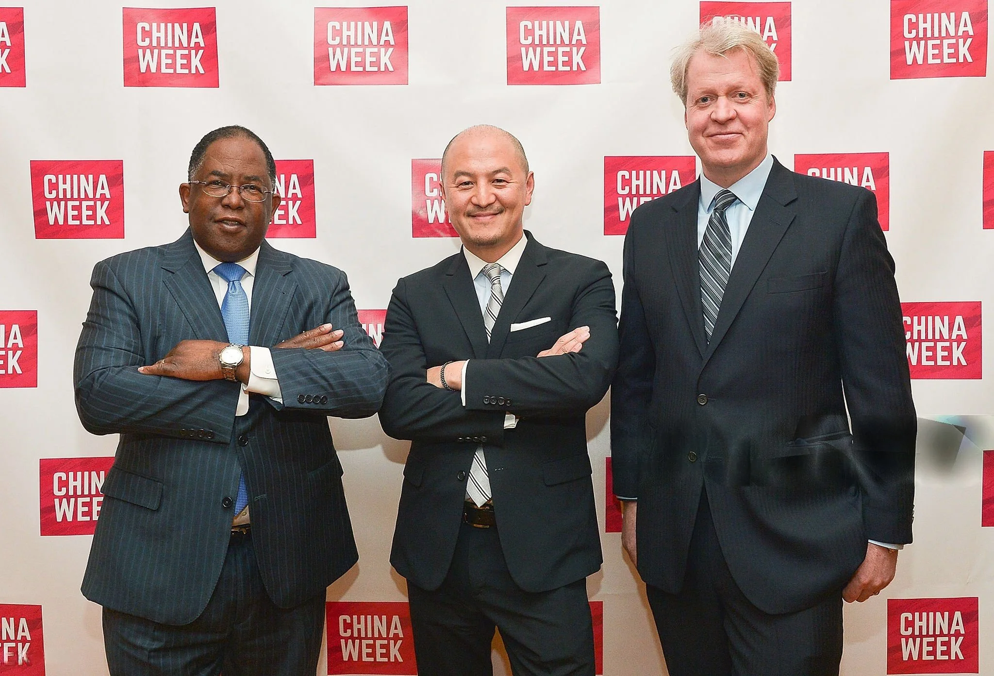 Three men in business suits standing in front of a backdrop with the red and white 'China Week' logo, arms crossed, smiling at the camera.