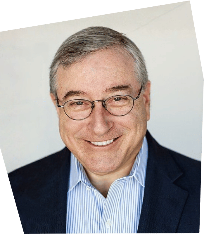 A smiling middle-aged man with gray hair, glasses, wearing a dark blazer and a blue and white striped shirt, against a plain white background.