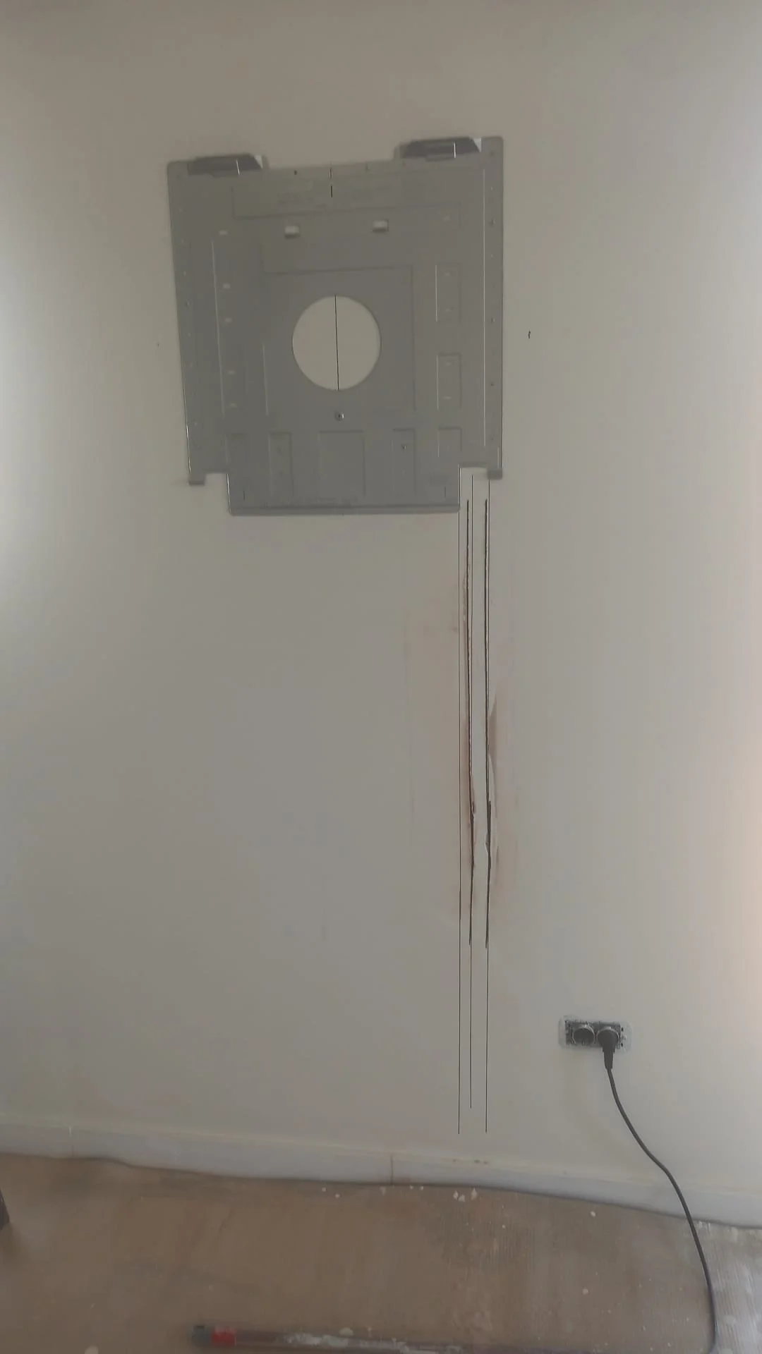 Hooked up wall plate with a black power cord plugged into an outlet underneath, with the cord hanging down a long crack in the wall.