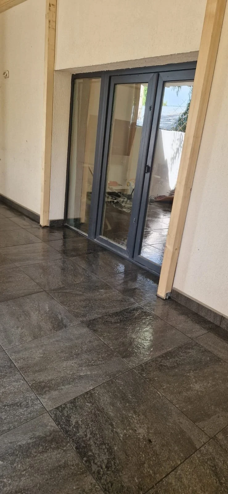 Interior space with newly installed sliding glass door and dark tile flooring, partially unfinished wall with wooden framing.