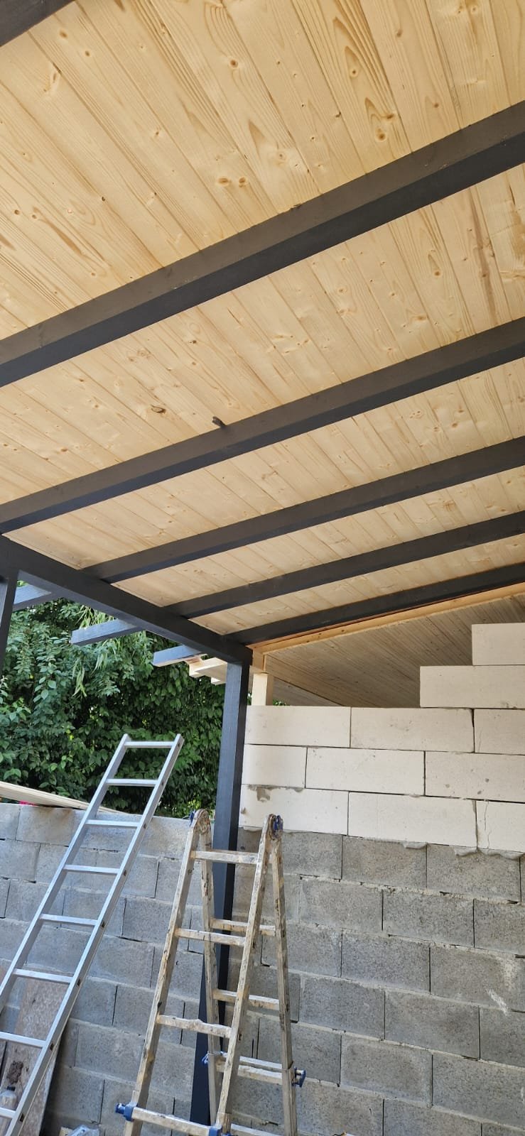 Under construction with ladders, cinder block wall, wooden ceiling, and metal supports in a building site.