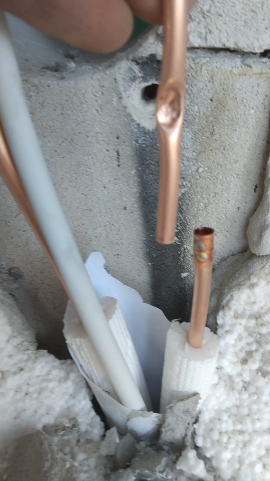 Close-up of copper and white electrical wires inside a wall with insulation and drywall around.