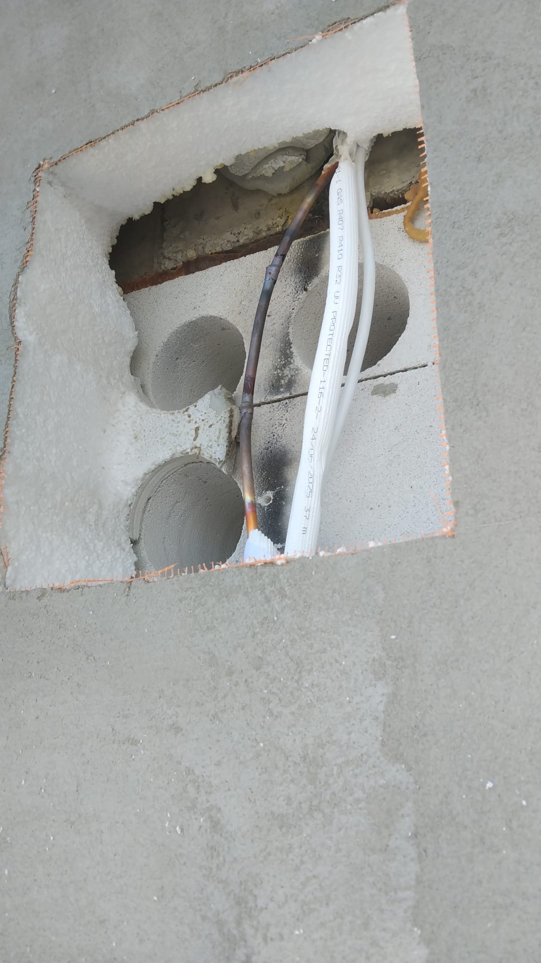 A close-up of an electrical outlet box embedded in a concrete wall with exposed electrical wires.