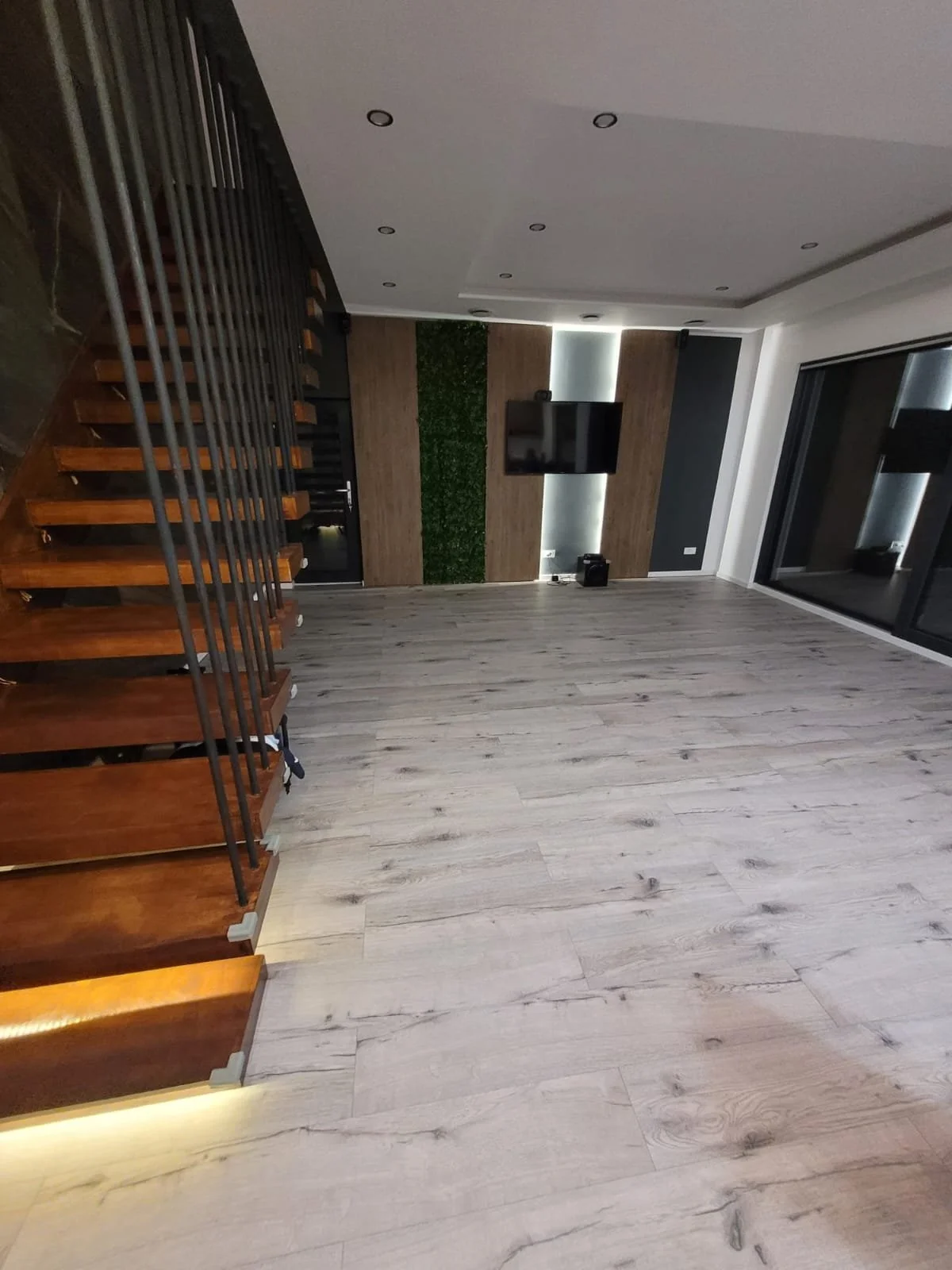 Empty living room with light-colored wooden floors, a wall-mounted world, a television, and a sliding glass door.