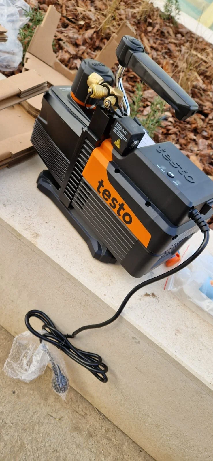 Testo vacuum pump placed on a concrete ledge with cardboard boxes and dried leaves in the background.