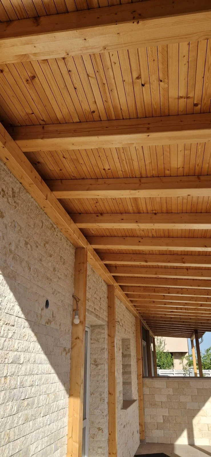 Wooden ceiling beams and paneling on the ceiling of a covered outdoor patio area of a house.