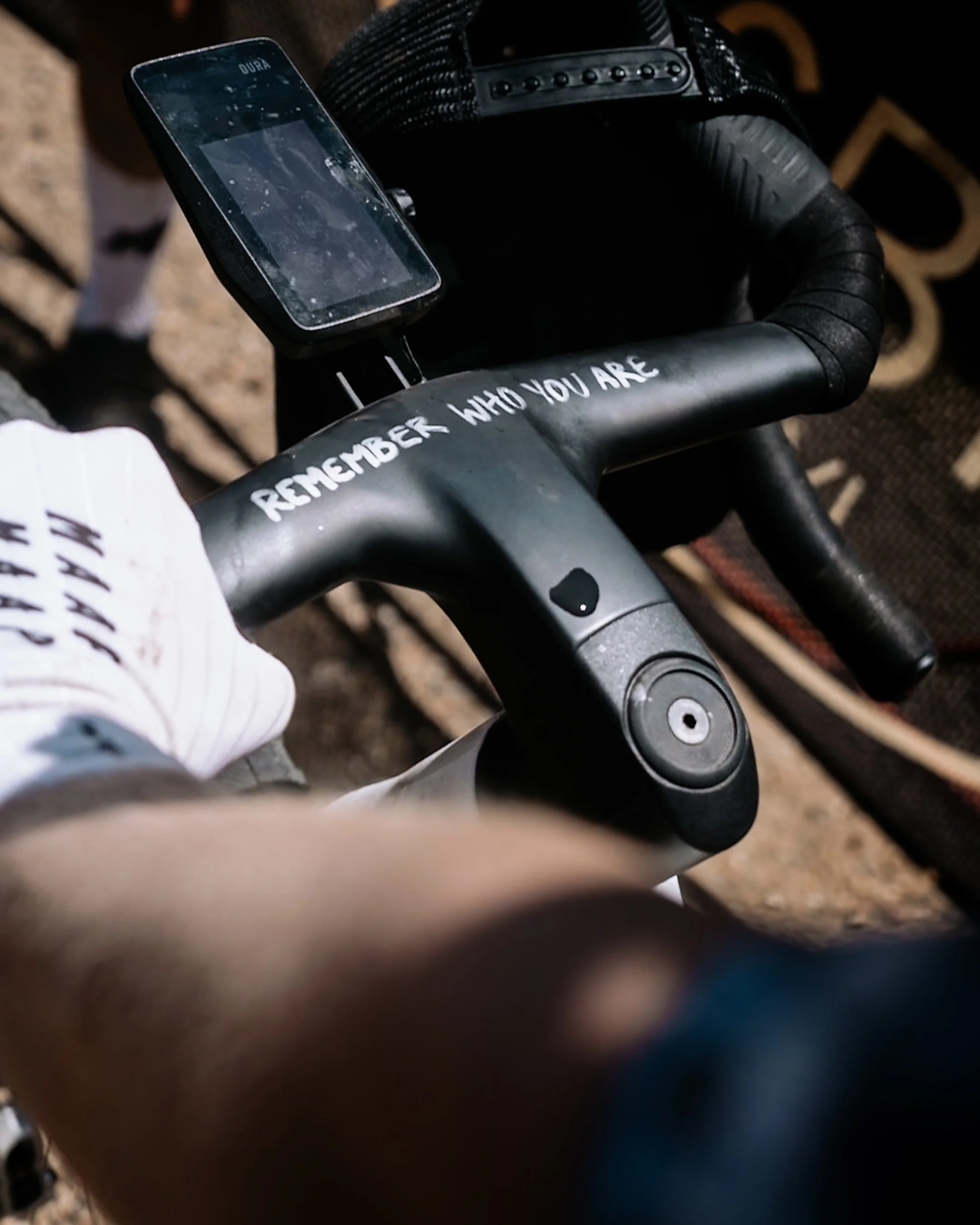 Close-up of a person's hand on the handlebar of a bike or scooter, with the words 'REMEMBER WHO YOU ARE' written on it.