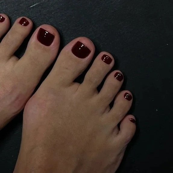 Close-up of a person's feet with toes painted in dark red nail polish, resting on a black surface.