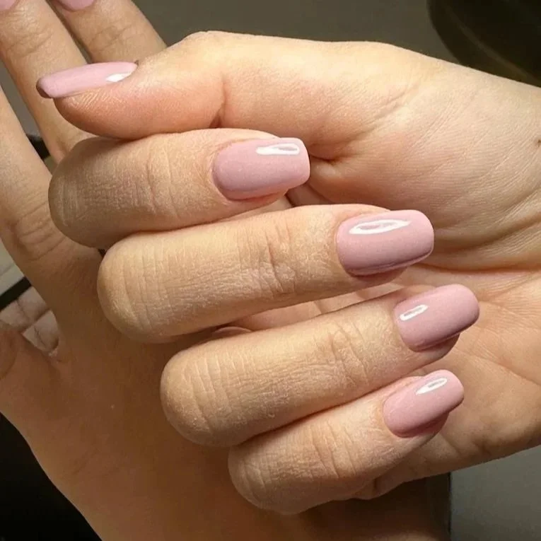 Close-up of a person's hand with manicured nails painted in light pink with a shiny finish.