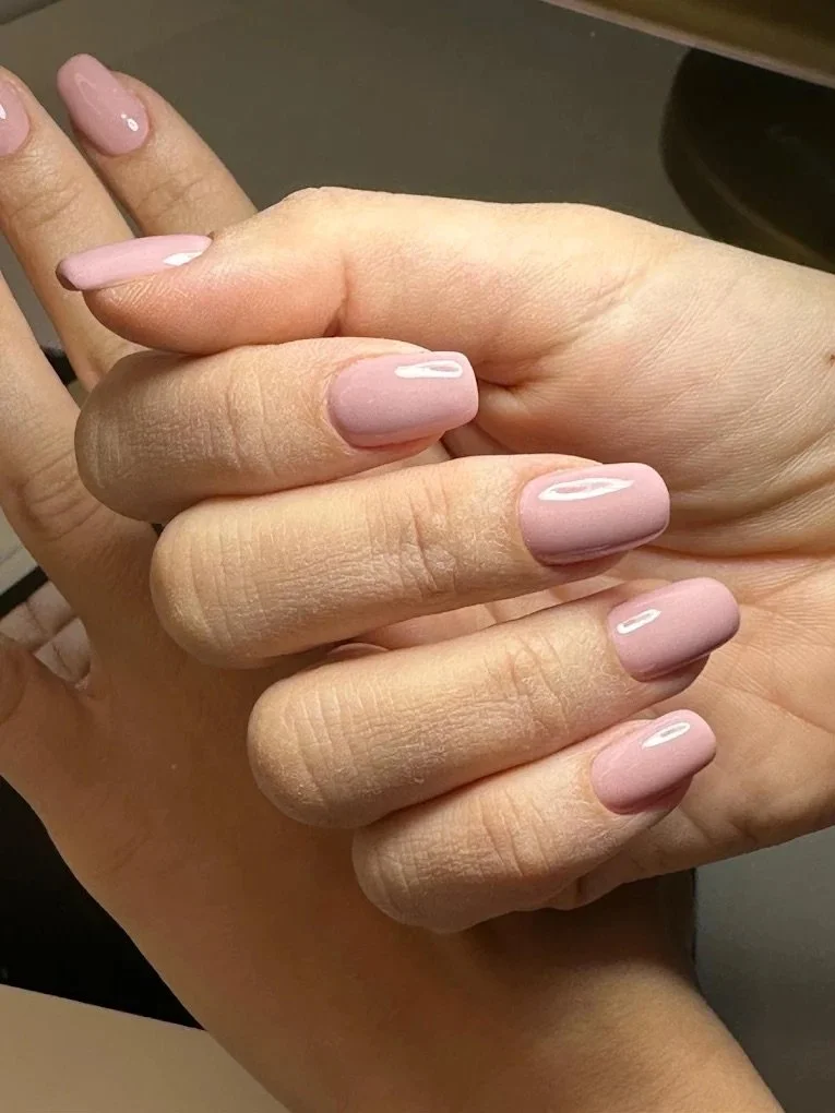 Close-up of a hand with neatly manicured nails painted in a soft pink color, held gently against a dark background.