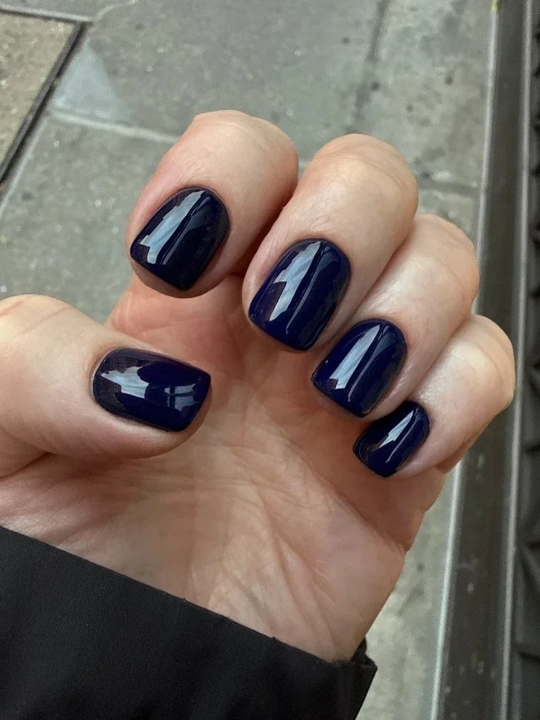 Hand with dark blue painted nails, held in front of a tiled floor background.
