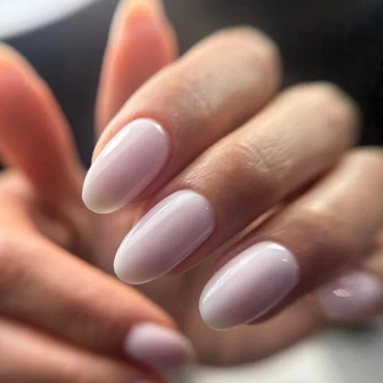 Close-up of a hand with manicured nails painted in a light, neutral color.