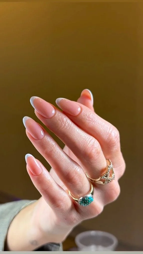 Close-up of a hand displaying three rings, with well-manicured fingernails and a blurred background.