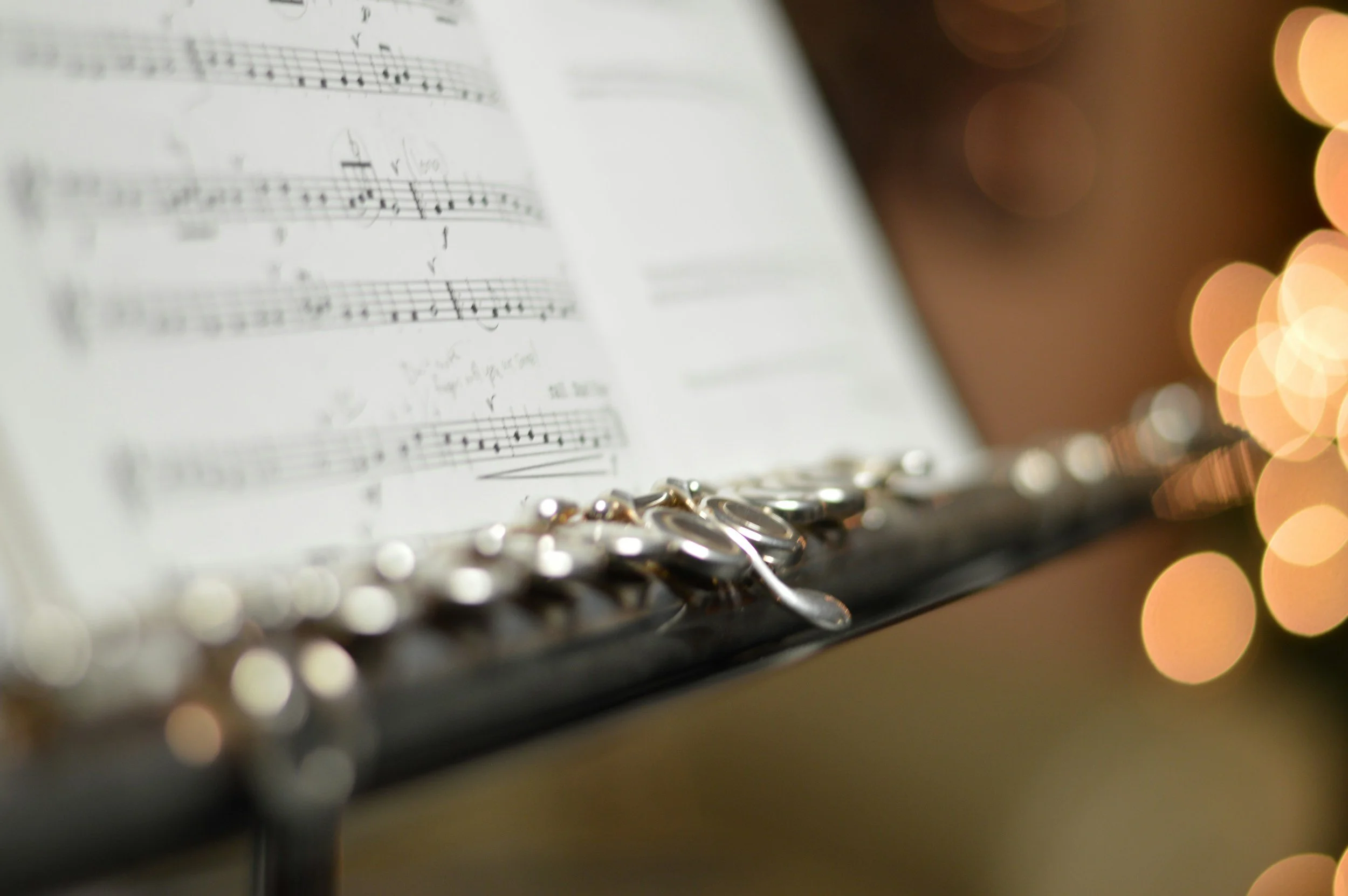 Close-up of a music stand with sheet music and a flute resting on it, with warm bokeh lights in the background.