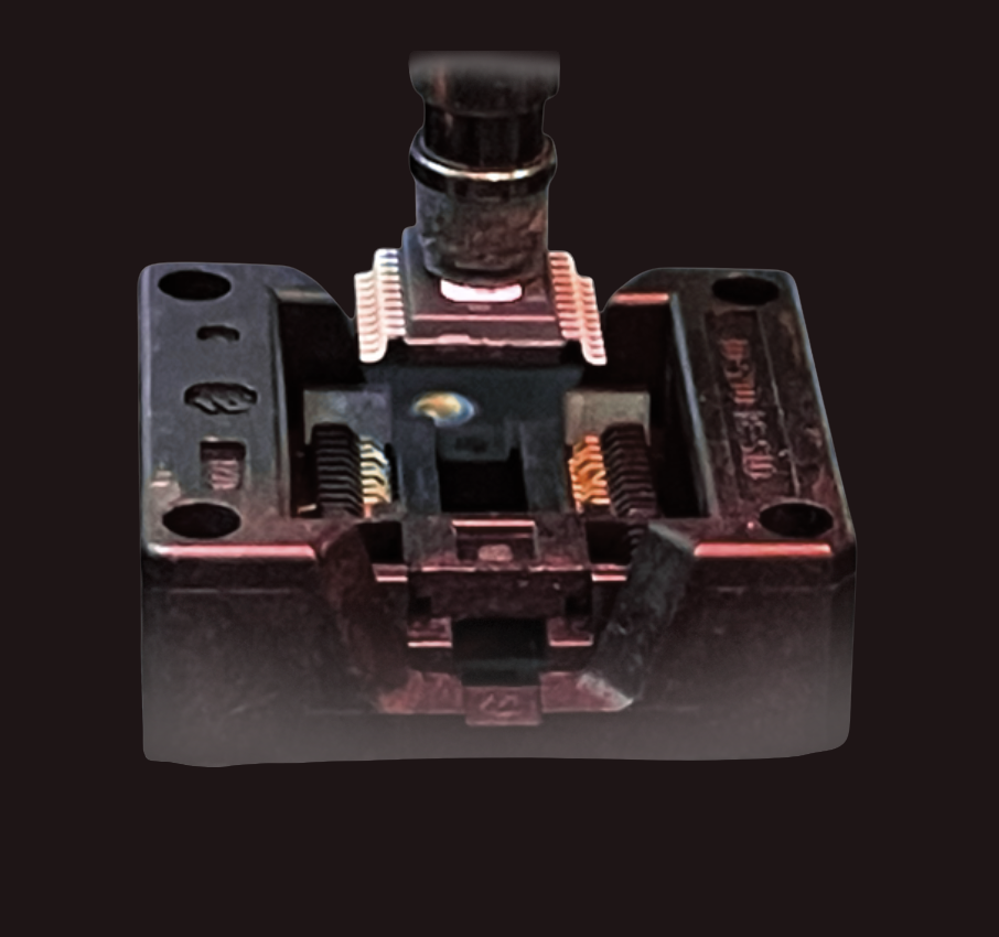 Close-up of a mechanical device with a black top and a metallic base, possibly part of a machine or tool, on a dark background.