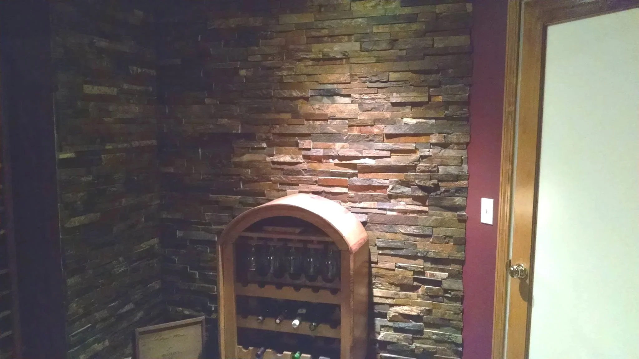 Interior of a wine cellar with a stone accent wall, a wooden wine rack holding several bottles, and a frosted glass door.
