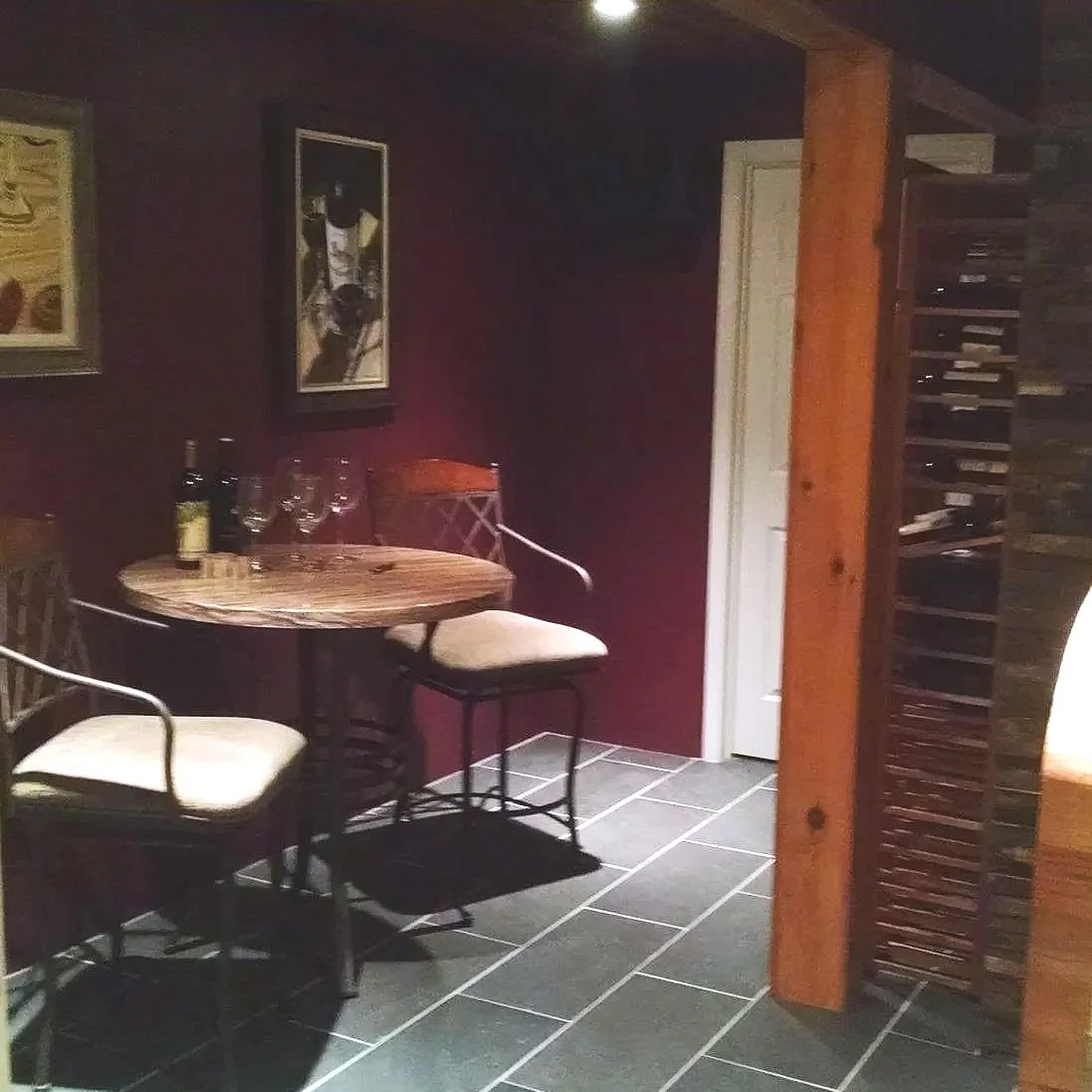 Interior of a wine cellar tasting area with a stone accent wall, a wooden wine rack holding several bottles, and a frosted glass door.