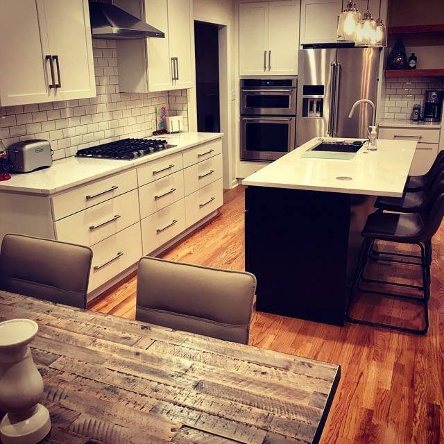 Modern kitchen with custom white cabinets, a white marble countertop, stainless steel appliances, and hardwood flooring.
