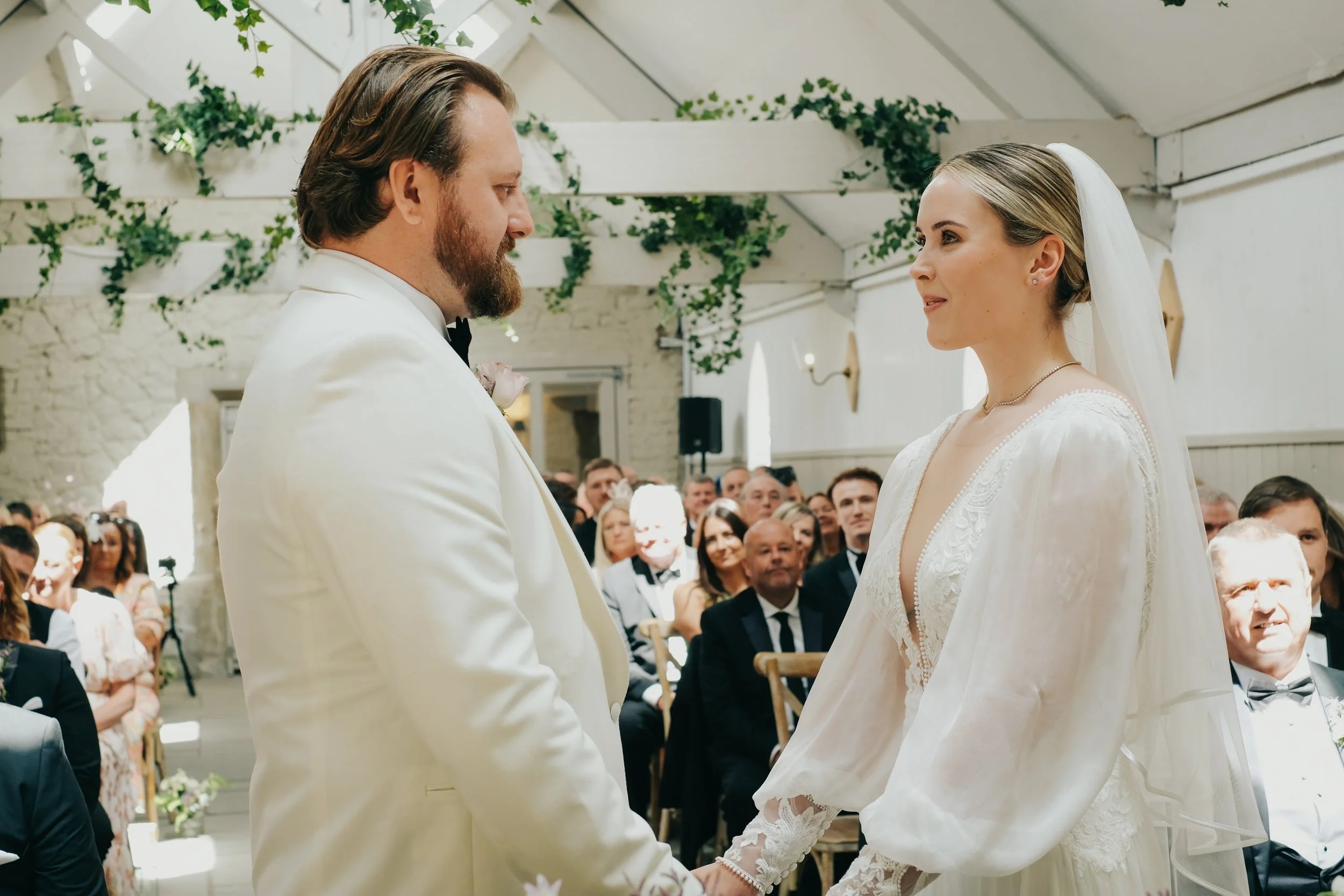 Bride and groom exchanging vows during wedding ceremony in a decorated indoor venue with guests seated in the background.