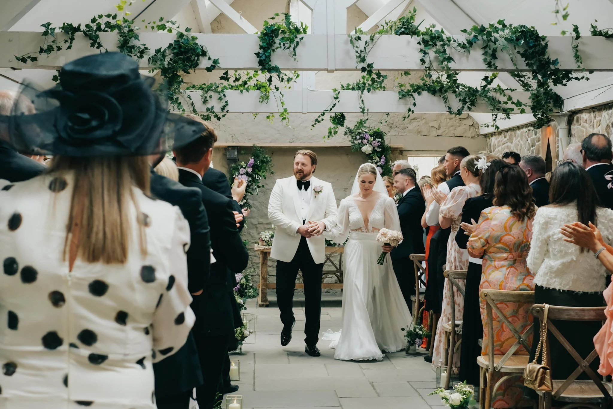 Bride and groom walking down the aisle at their wedding ceremony as guests applaud.