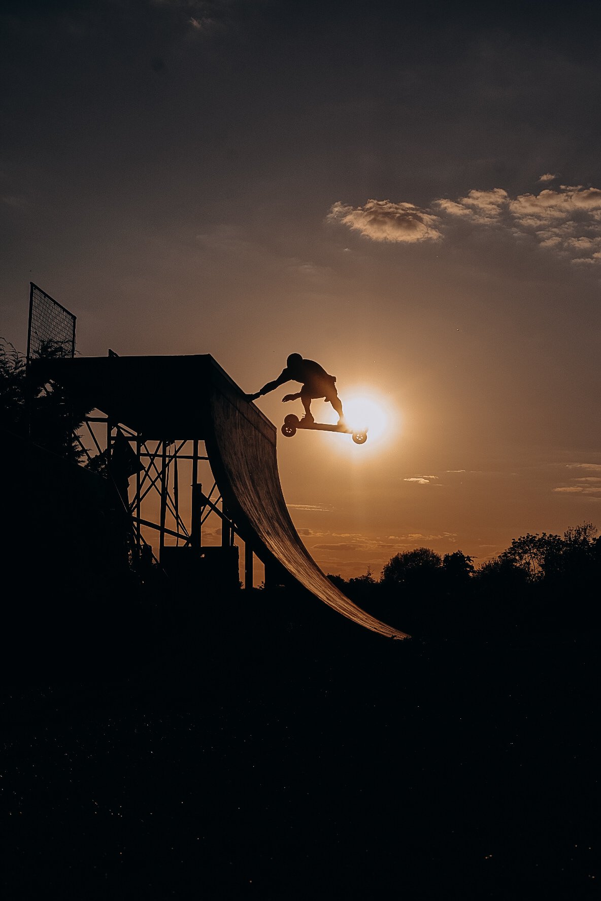 A silhouette of a person on a skateboard at the top of a ramp during sunset.