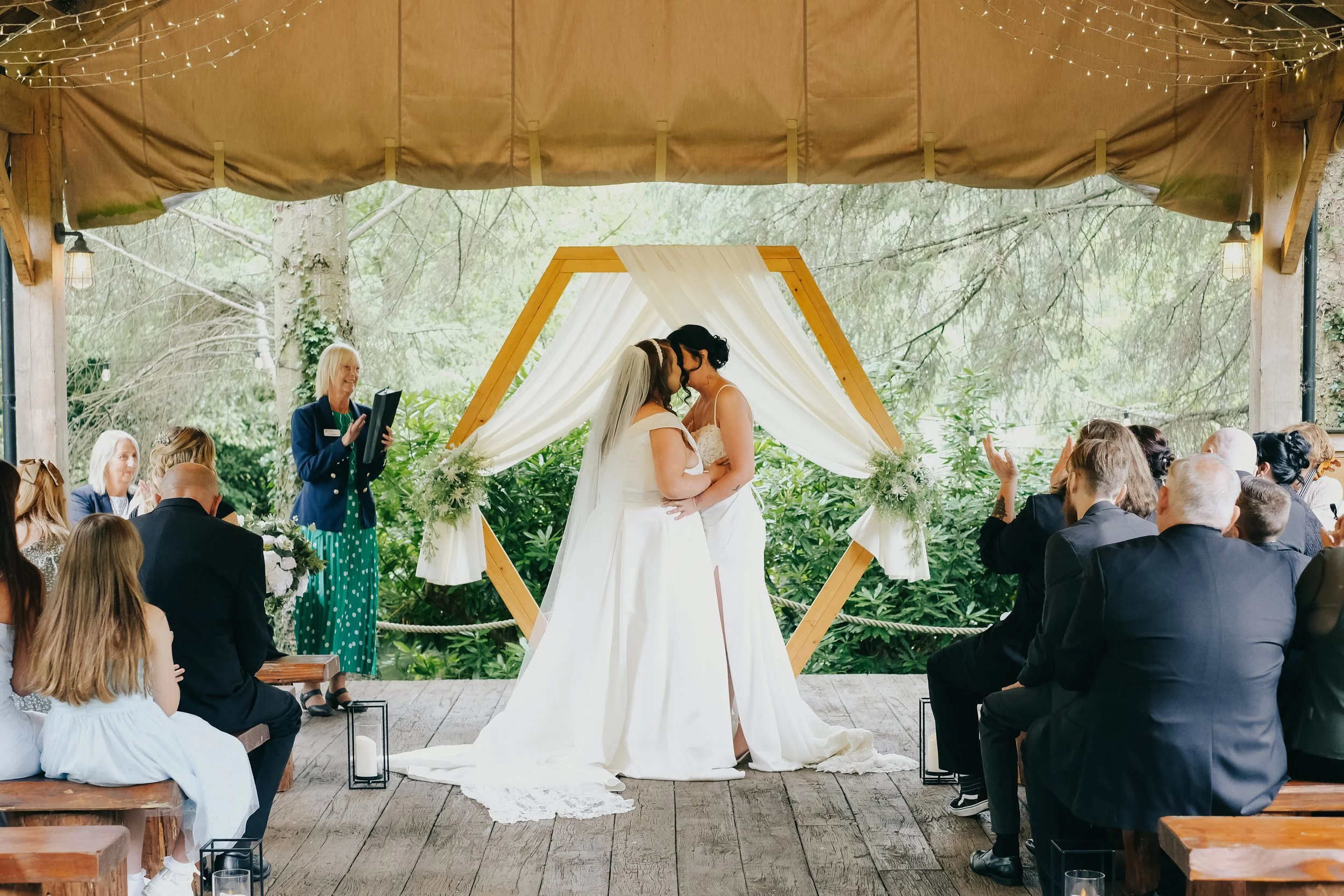 Two brides kissing at their wedding ceremony. Natural, rustic, relaxed documentary wedding photography image by female Lake District and Northumberland wedding and elopement photographer, Sarah.