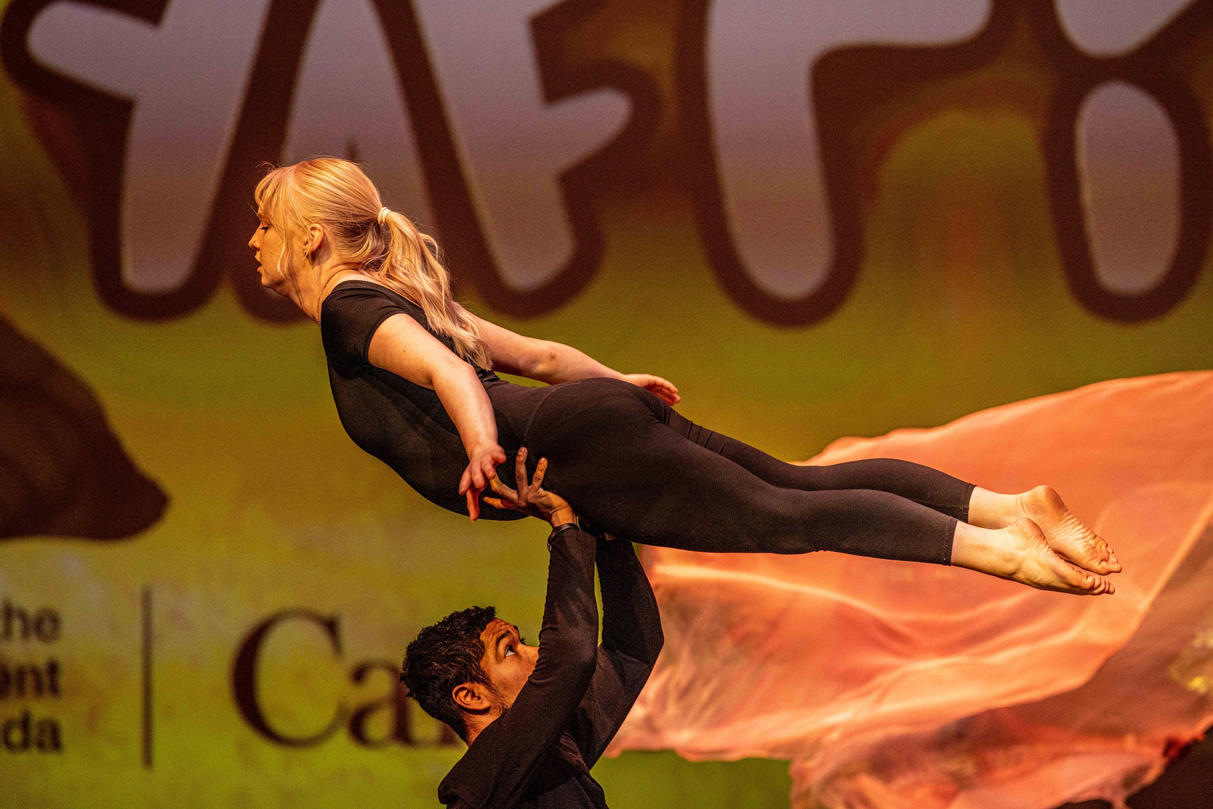 A woman being lifted in the air with a man during a performance or show on stage.