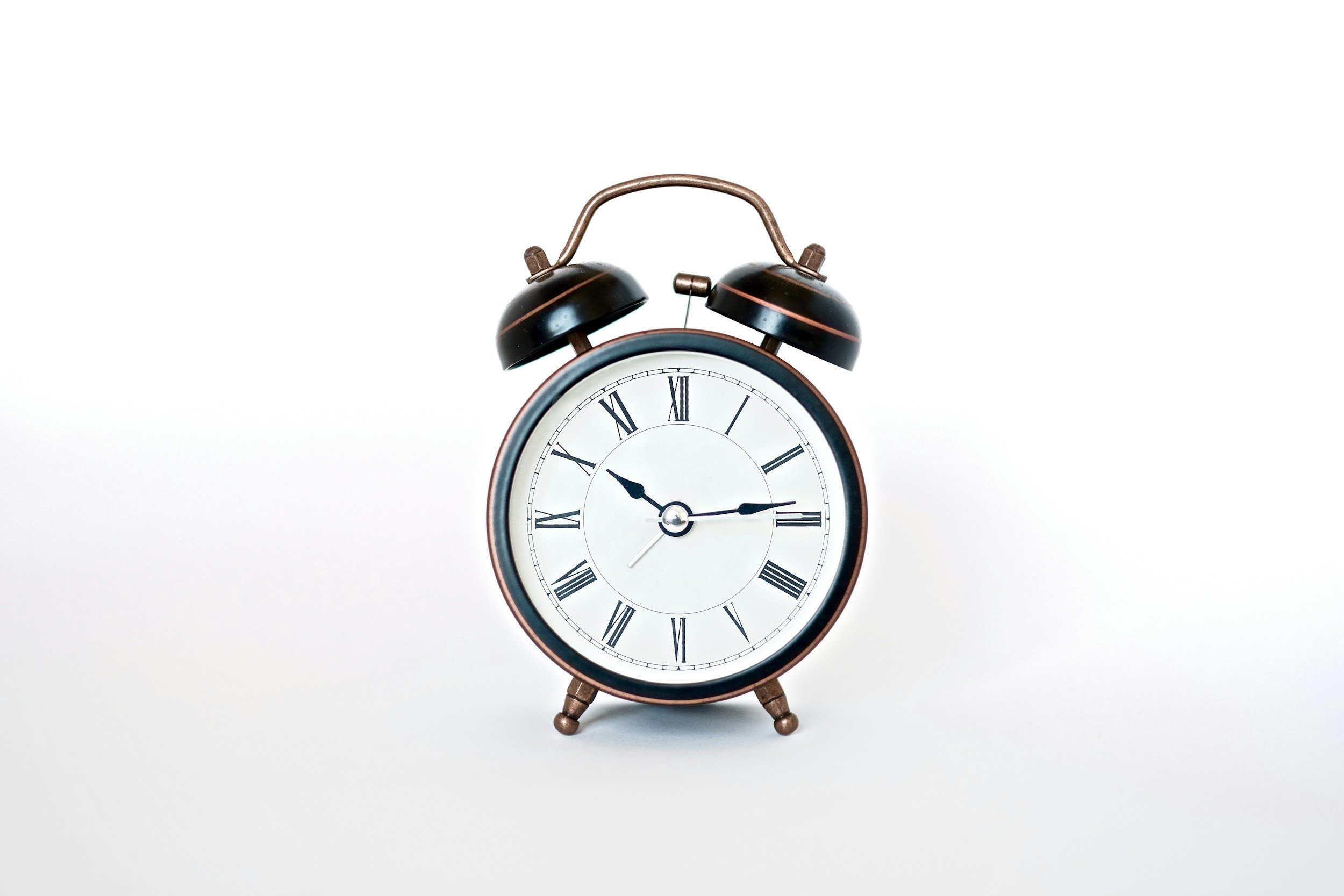 A vintage-style alarm clock with Roman numerals, showing approximately 9:14, against a plain white background.