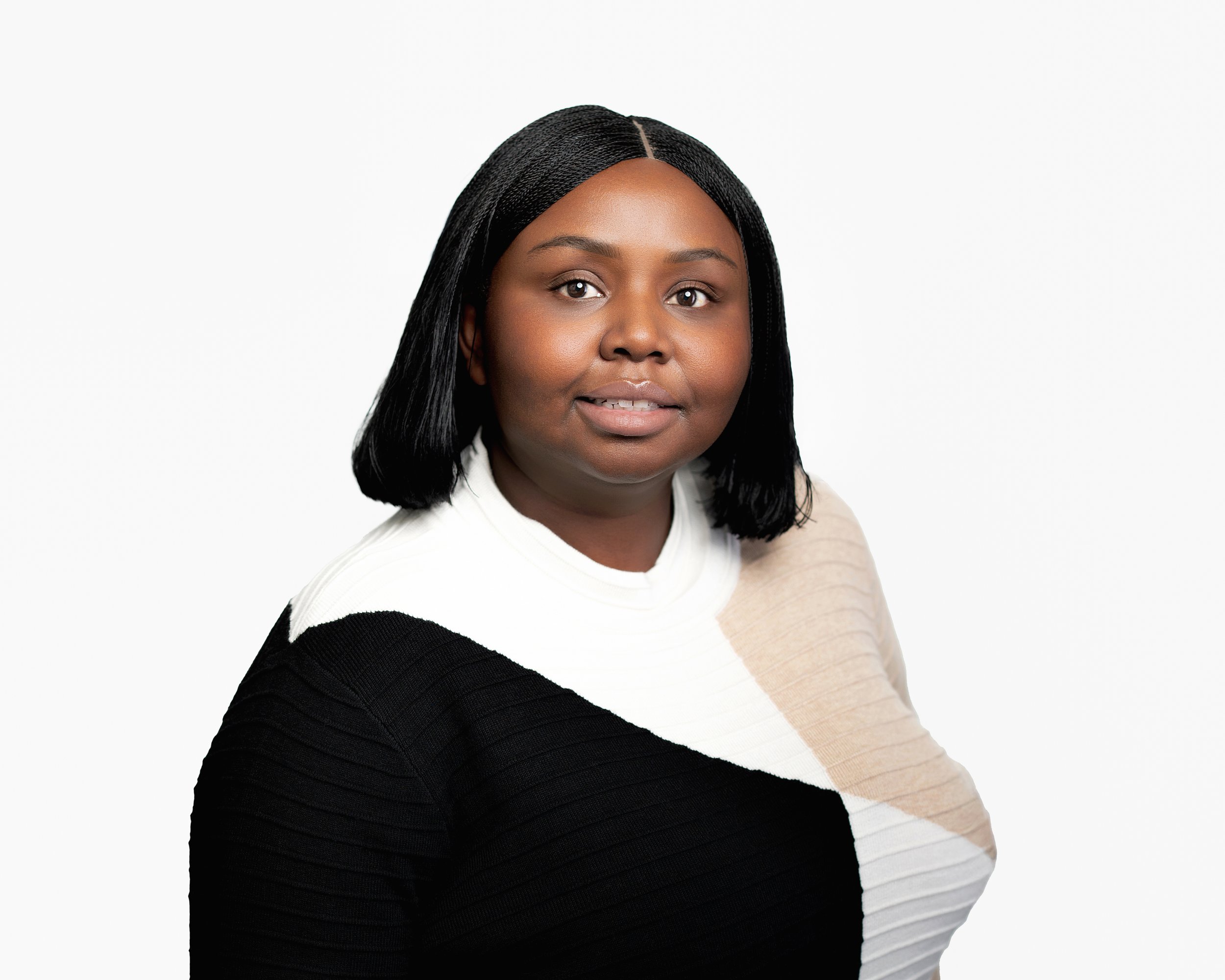 Portrait of a woman with black hair, wearing a color block sweater with black, white, and beige sections, against a plain white background.