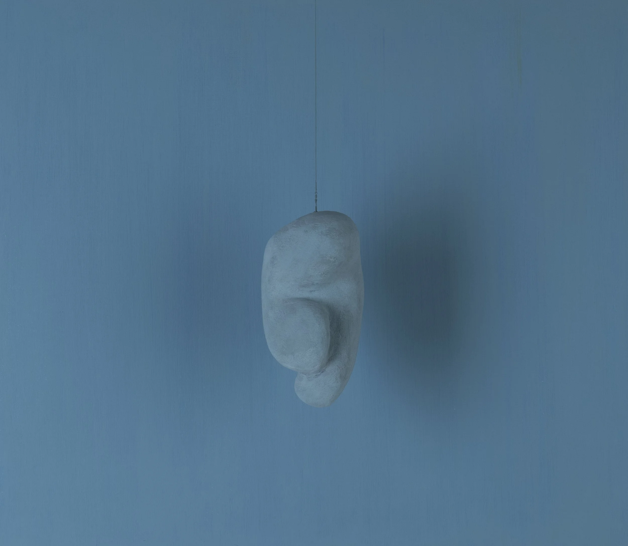 Sospensione decorativa a forma di orecchio in cemento, appesa a un filo, con sfondo blu.