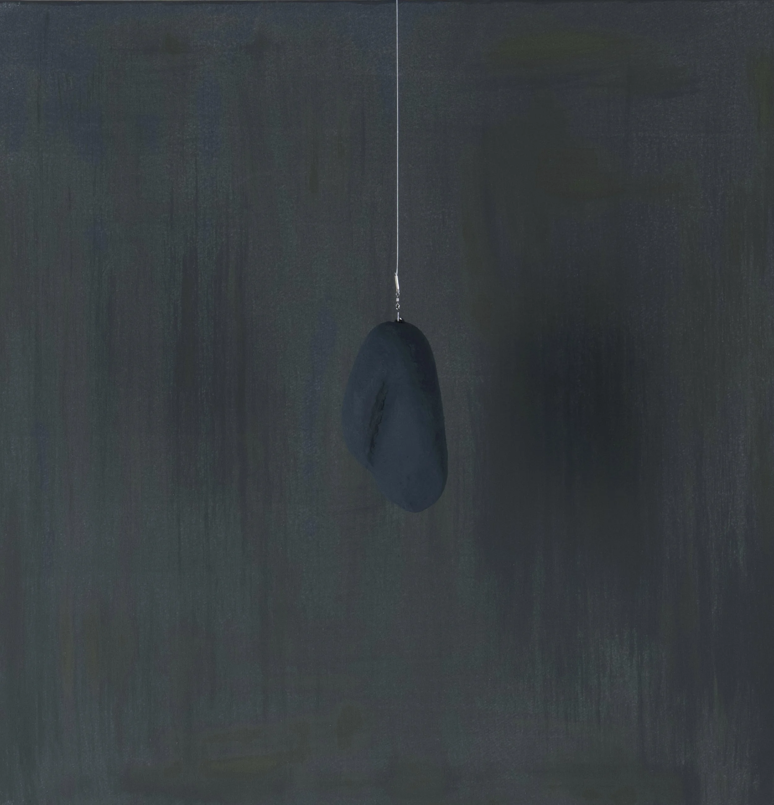 Pietra nera sospesa con filo sottile contro uno sfondo scuro