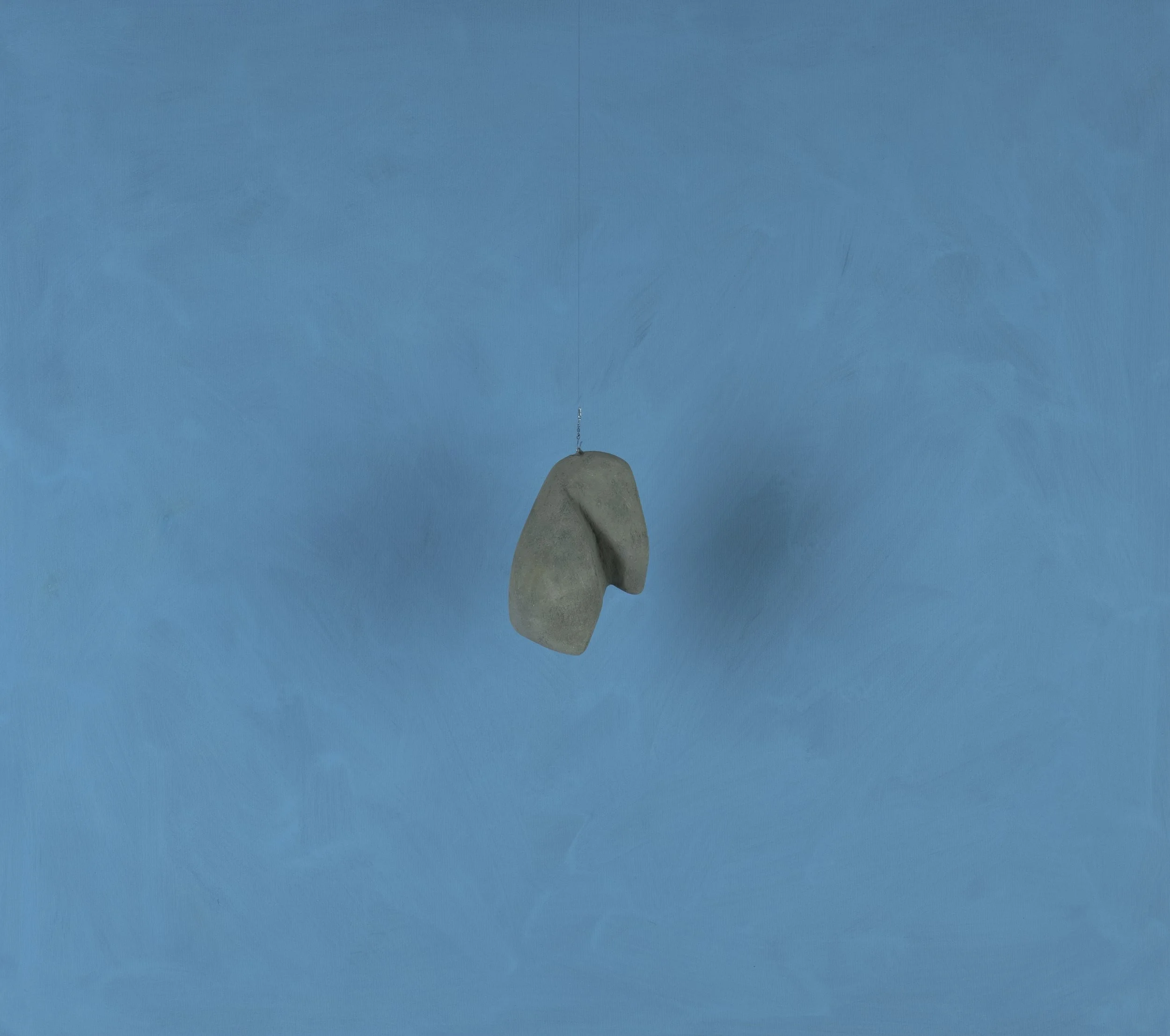 Sospensione di un sasso su una parete azzurra