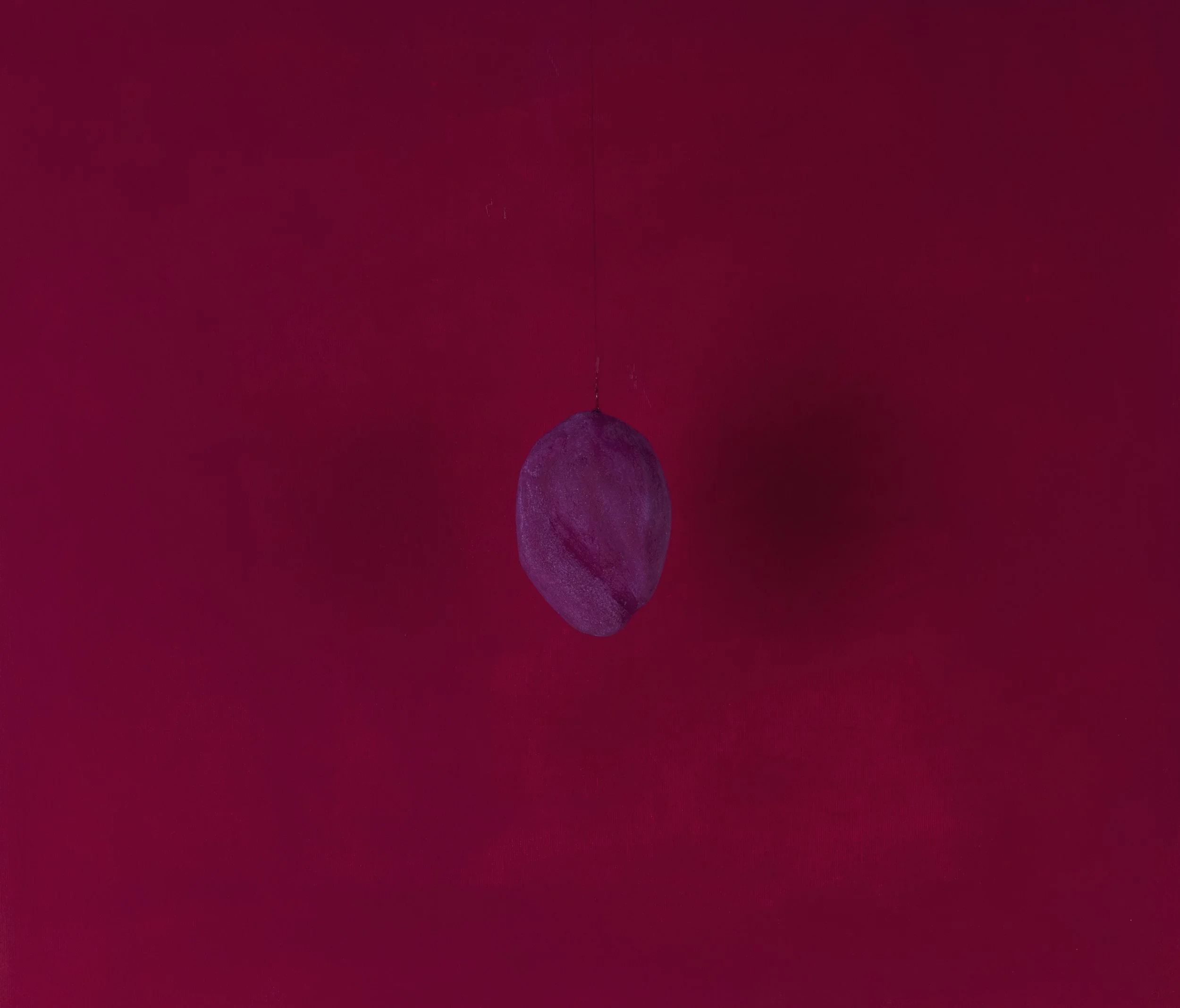 Oggetto sospeso di forma rotonda, colorato di viola, contro uno sfondo rosso.