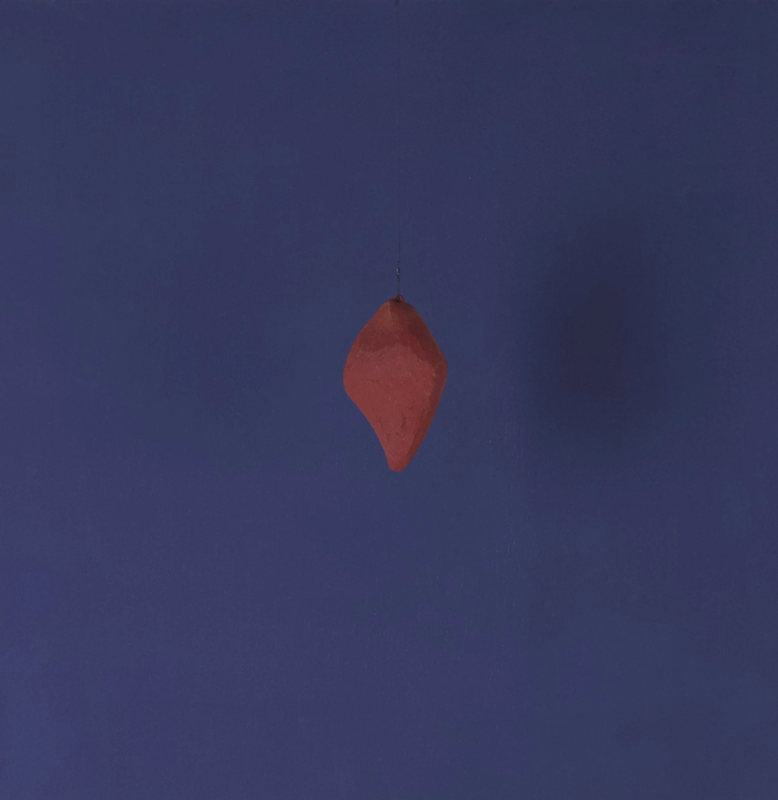 Un oggetto arancione a forma di diamante appeso a una linea sottile contro uno sfondo blu scuro.