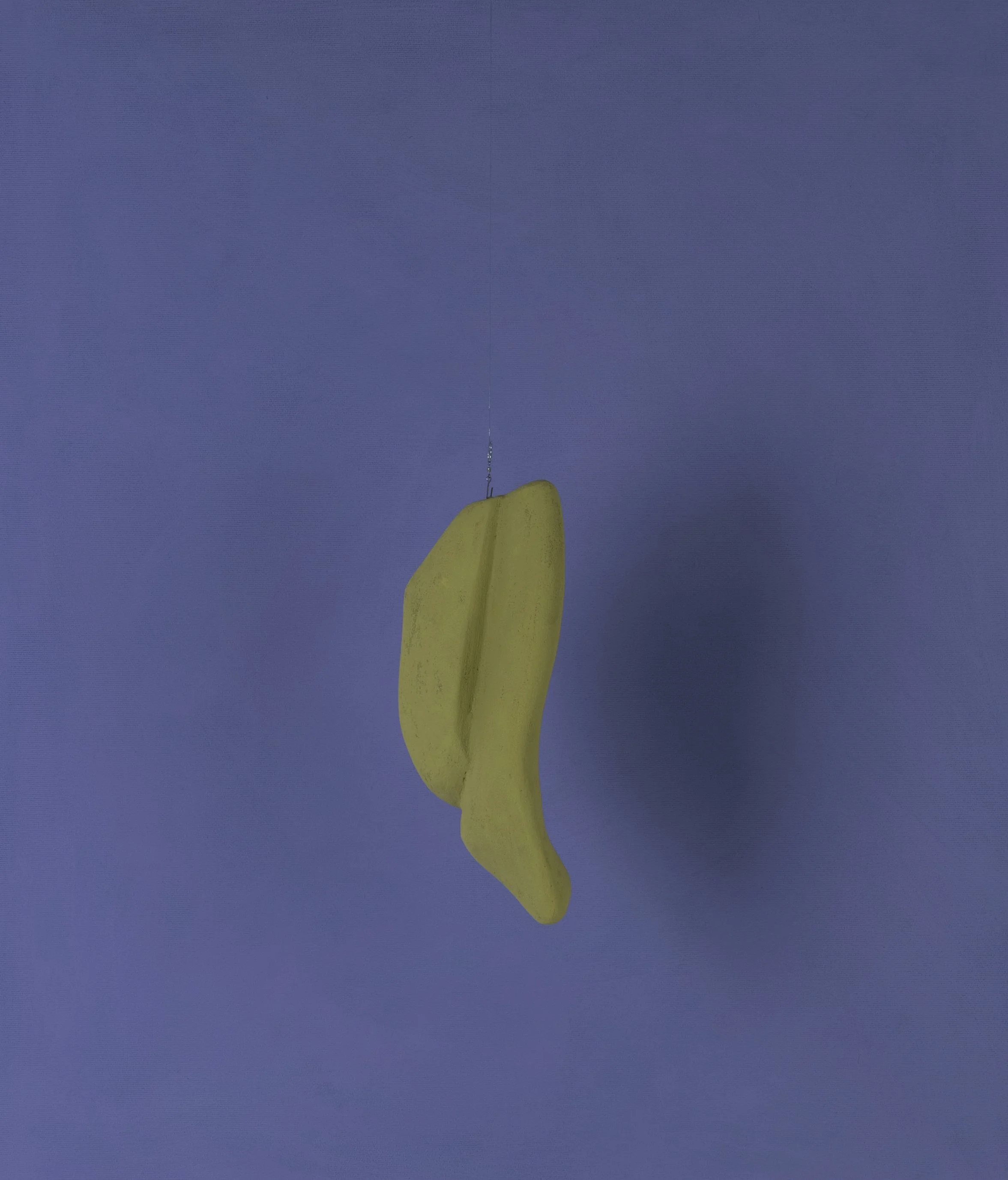 Una sedia di plastica gialla appesa a una corda contro uno sfondo blu.