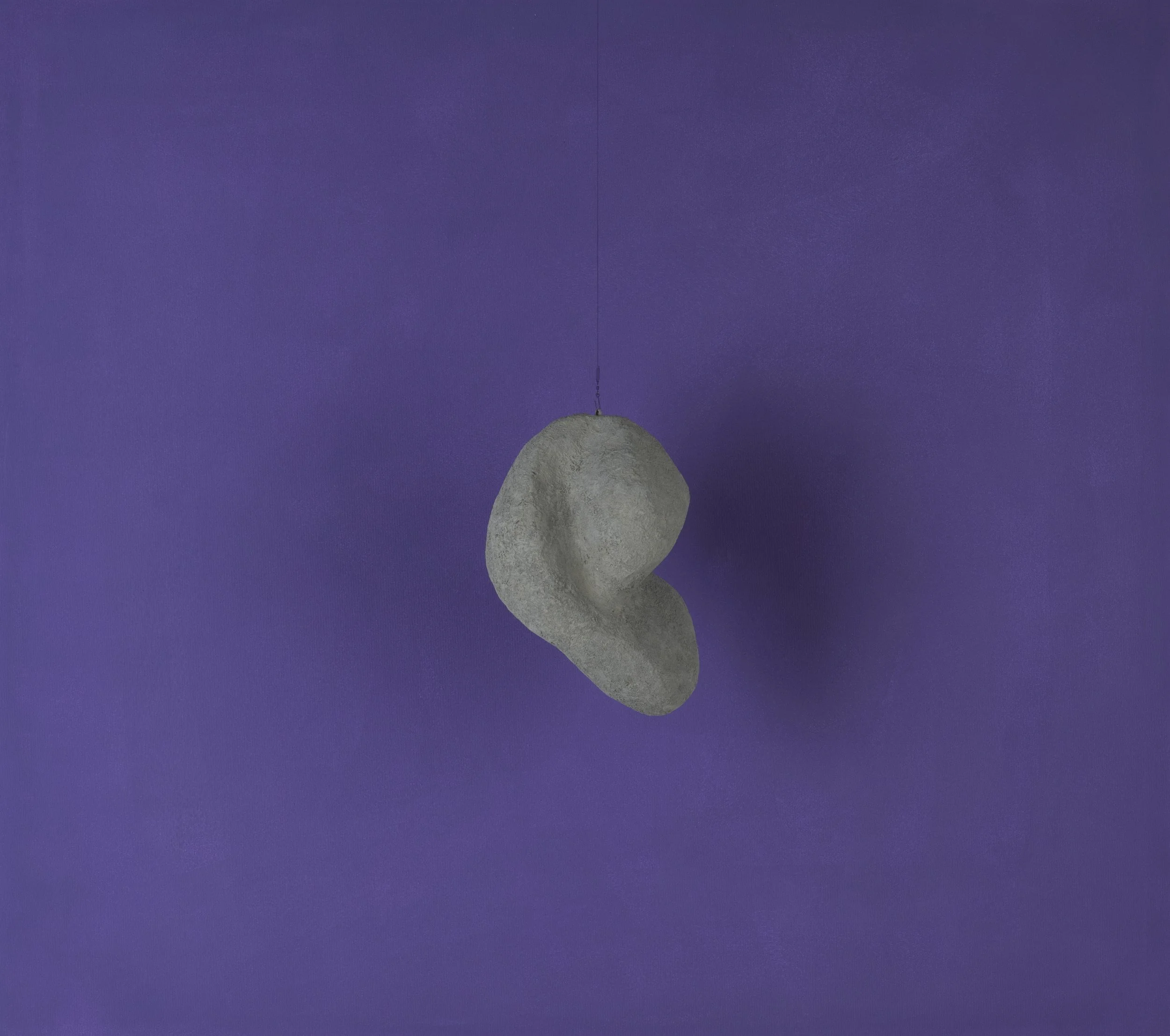 Un ciondolo di pietra grigia sospeso contro una parete viola