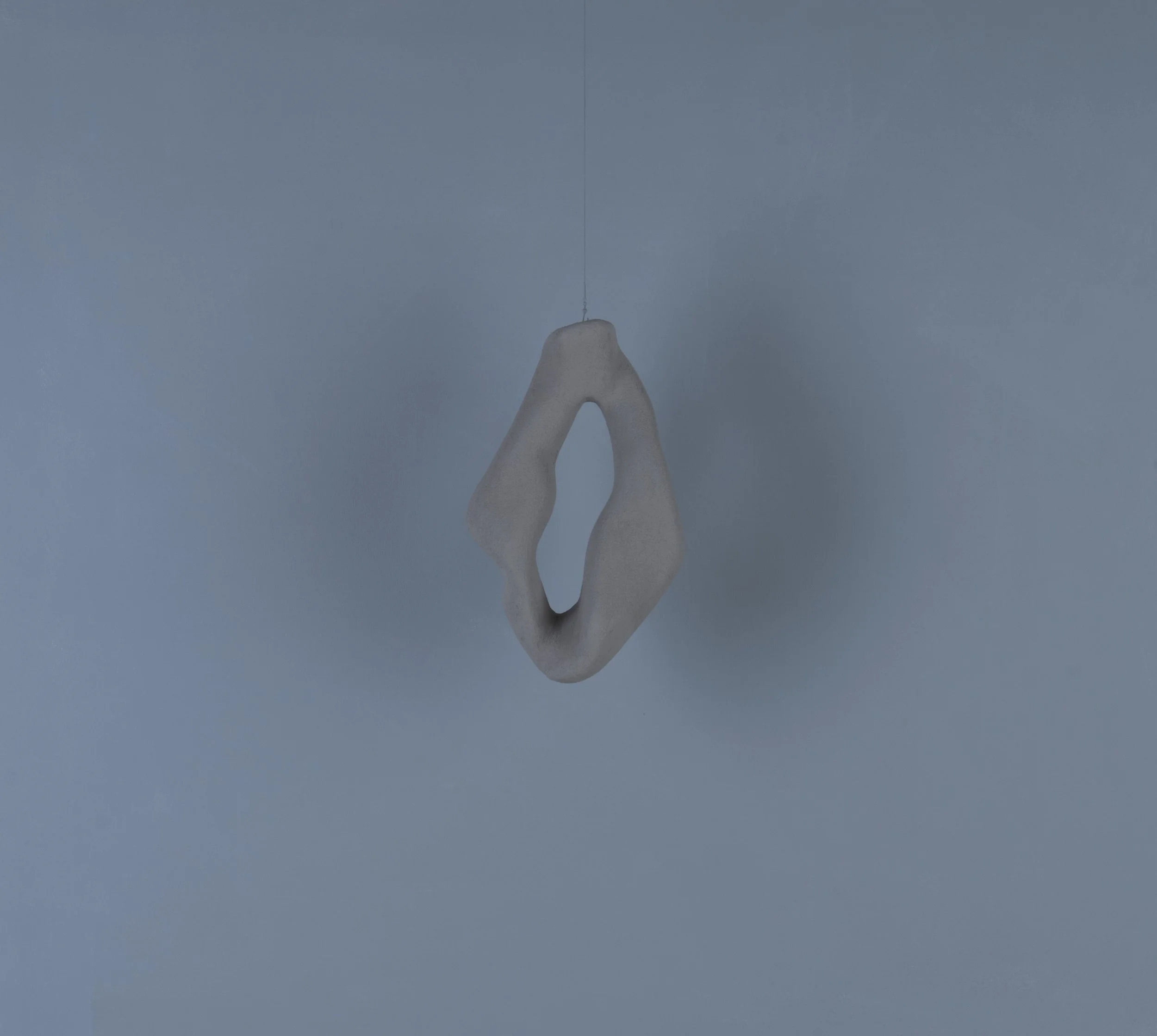 Oggetto decorativo sospeso di forma astratta, posizionato contro una parete blu chiaro.