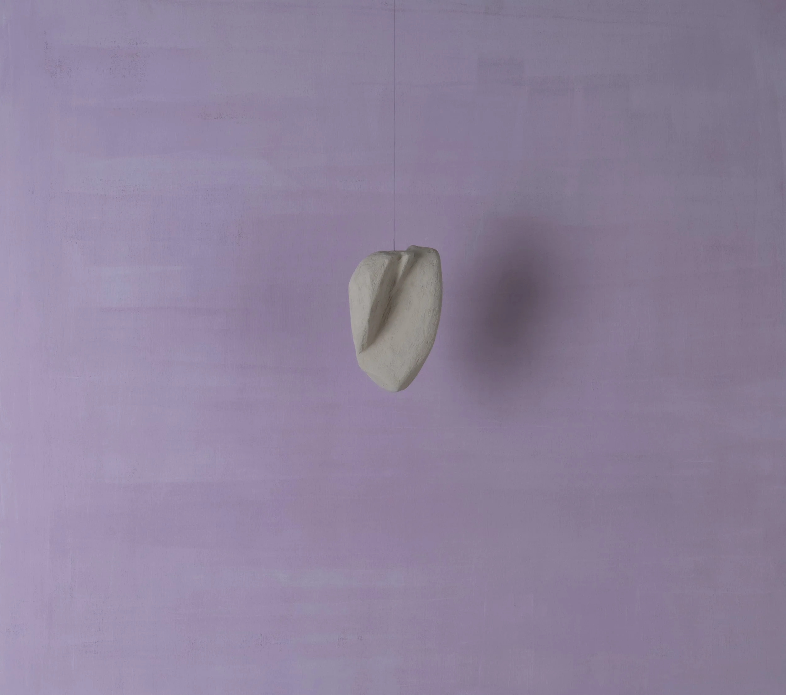 Una piccola scultura bianca sospesa in aria su uno sfondo viola chiaro.